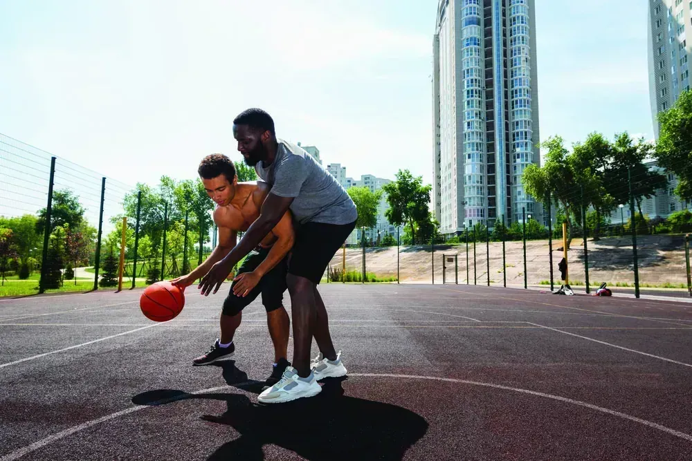Two players on the outdoor basketball court in late afternoon light
